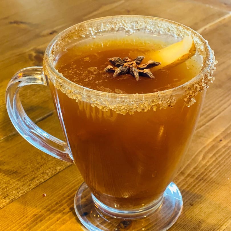 A Caribbean hot toddy in a clear mug, garnished with star anise and a citrus slice.