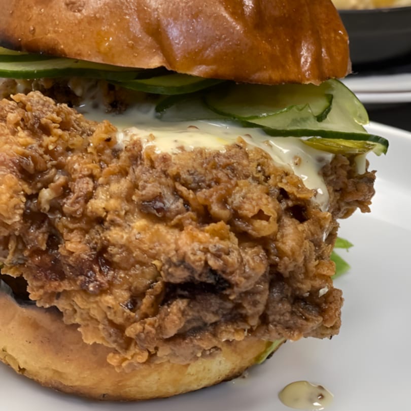 Crispy fried chicken sandwich with pickles and creamy sauce on a brioche bun, from An Artistic Taste.