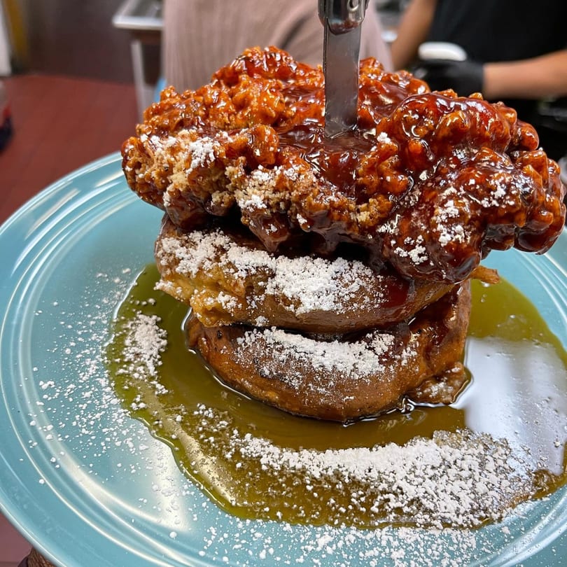 Fried chicken and waffles with syrup and powdered sugar, a knife stuck in the chicken.
