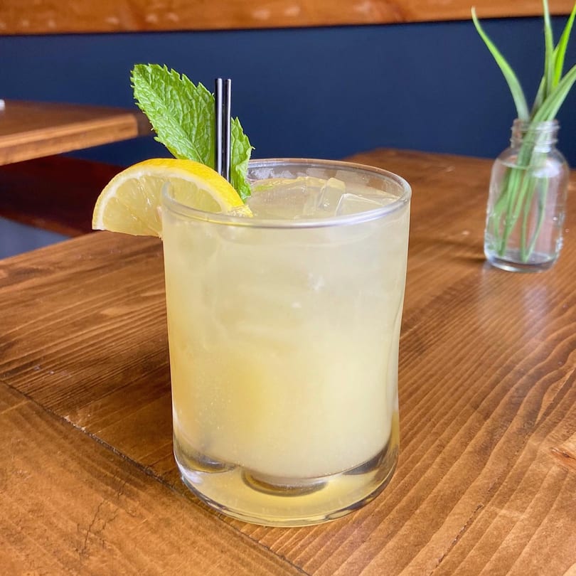 Refreshing Caribbean cocktail with lemon, mint, and straws on a wooden table.