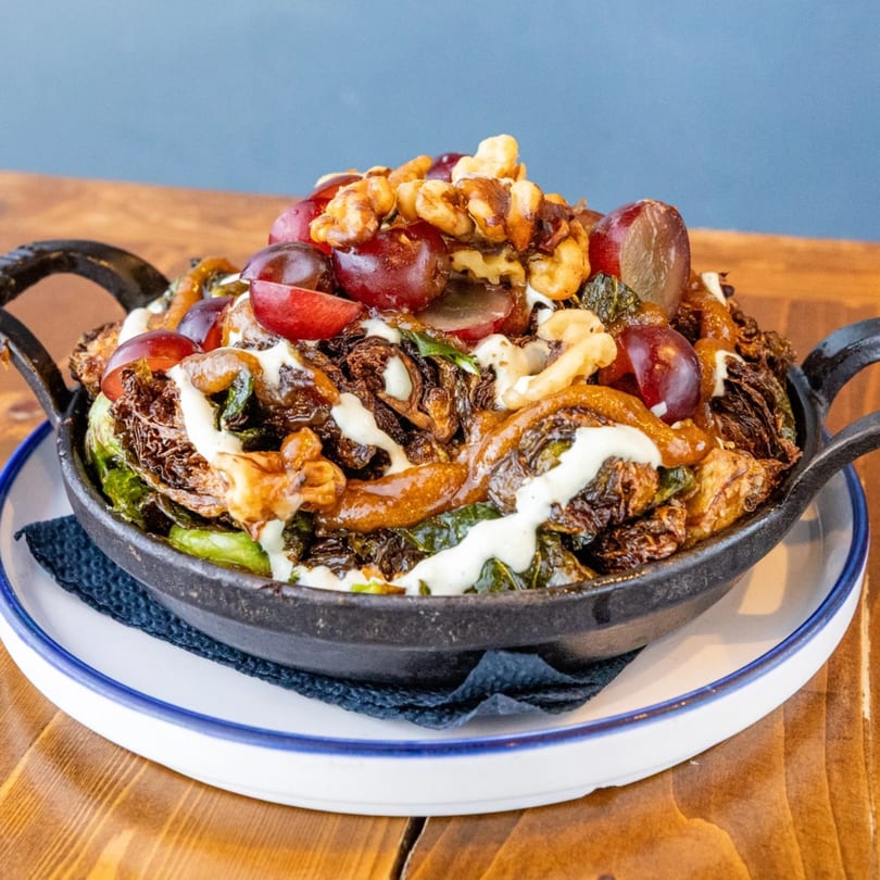 Crispy Brussels sprouts with grapes, walnuts, and a creamy sauce in a cast iron pan.
