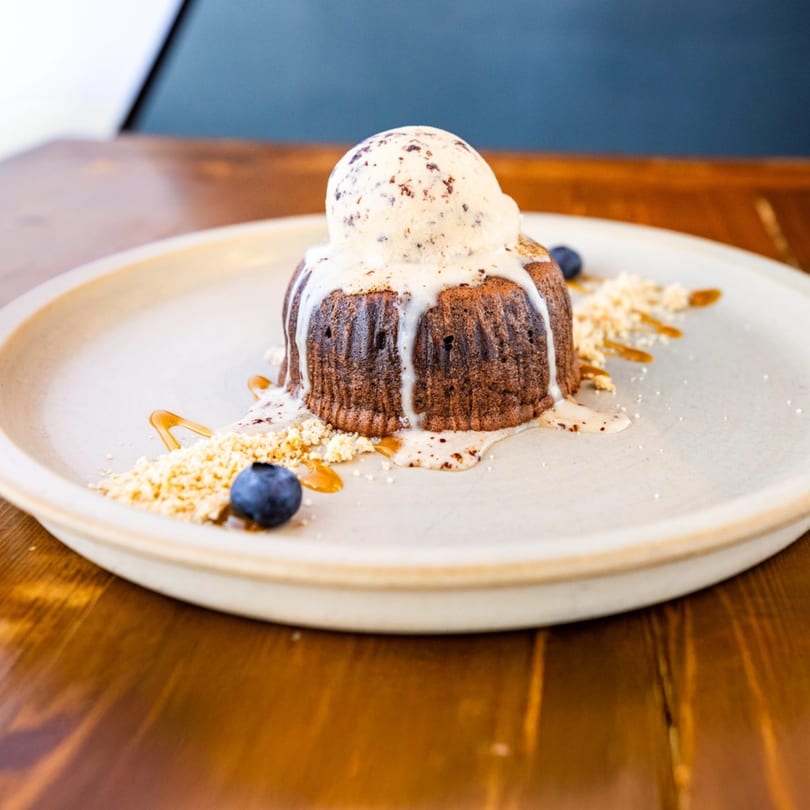Warm chocolate lava cake topped with vanilla ice cream, blueberries, and caramel drizzle.