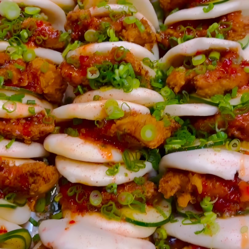 Close-up of Caribbean fried chicken bao buns with red sauce, cucumber, and green onions.