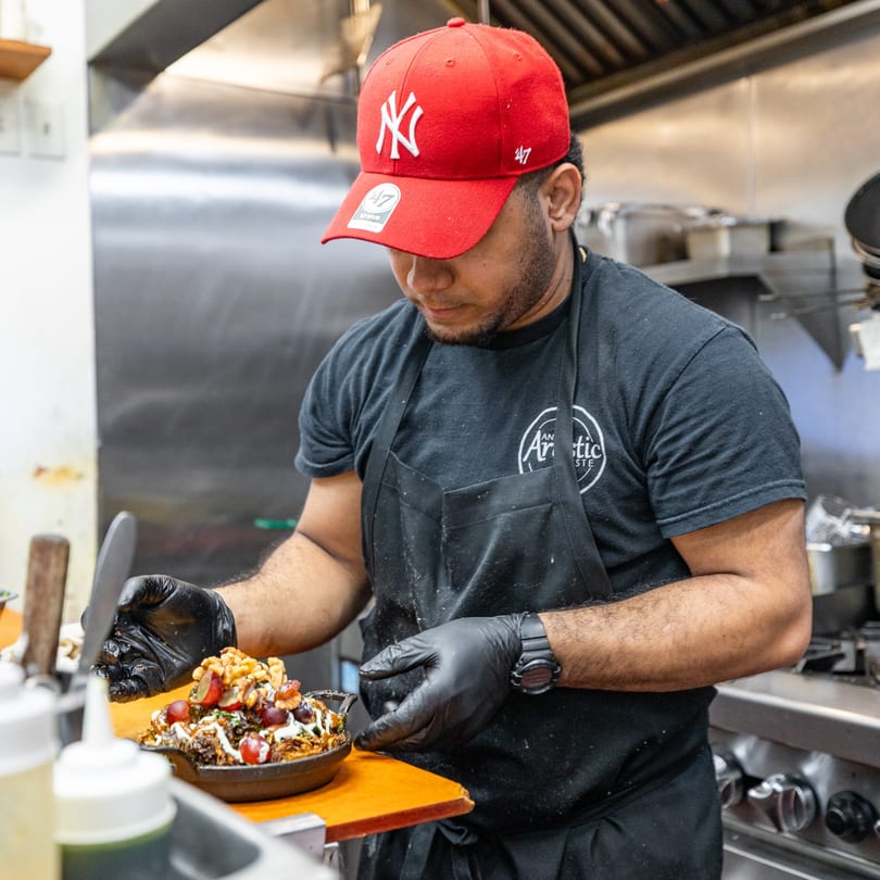 Chef in a red cap and black apron garnishing a Caribbean dish with fruit and nuts.