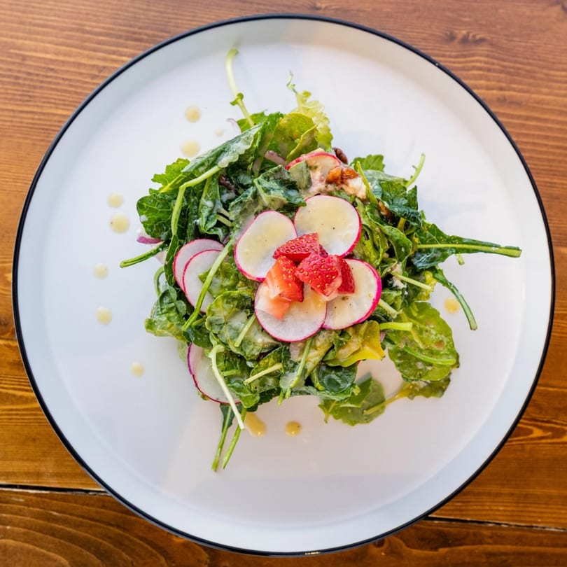 A fresh green salad with sliced radishes, strawberries, and a creamy dressing on a white plate.